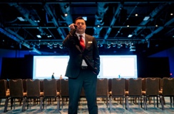 A man in a suit talking on a cell phone in a conference room while using Two-Way Radios for communication.