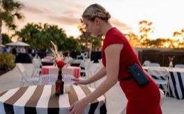 A woman in a red dress is setting up a table at an outdoor event while communicating via two-way radios.